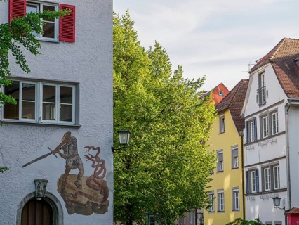 Historic building with mural of a knight and dragon surrounded by trees in an old town, lindau,