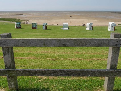 View over a green meadow with beach chairs and a wooden fence to a quiet sandy beach and the sea