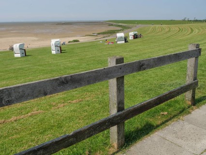 Meadow with beach chairs and a wooden fence along a path in front of a vast sandy beach and the sea