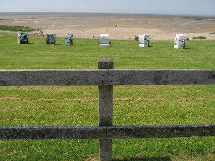 View over a green meadow with beach chairs and a wooden fence to a wide sandy beach and the sea in