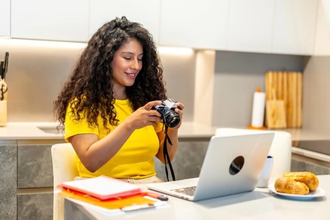 Beauty young latin female photographer checking the camera pictures working from home while eating