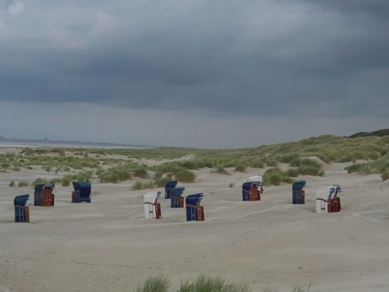 Scattered beach chairs on a sandy beach between grass and dunes under threatening clouds, Juist,