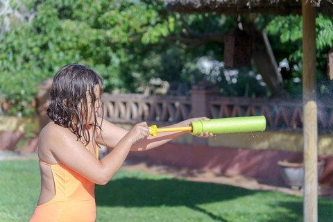 Cute girl in pink swimsuit playing in the pool with a foam gun toy