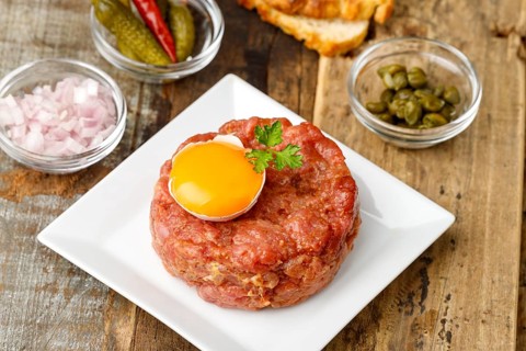 Steak tartare with open egg on wood