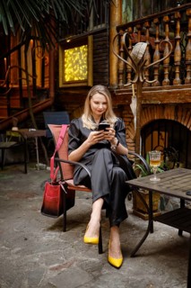 A stylish woman came to a wine bar, sat on the terrace and writes a message to her friends on her
