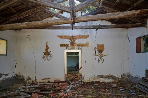 The wall of an abandoned building is covered with a peace message and several anarchy symbols,