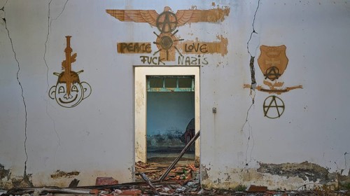 A graffiti with several artworks and a message of peace can be seen on a cracked white wall of an
