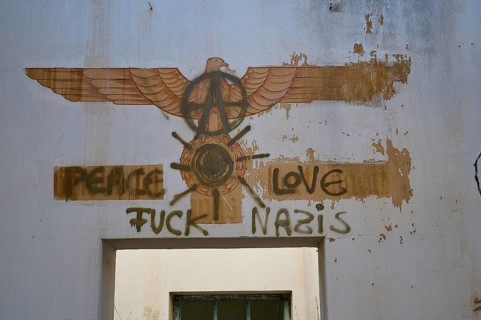 A graffiti with a message of peace and anarchy symbols can be seen on a cracked white wall in an