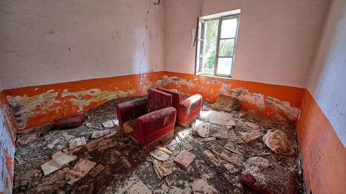 Abandoned room with worn red armchairs and orange-coloured walls. The floor is covered with dirt