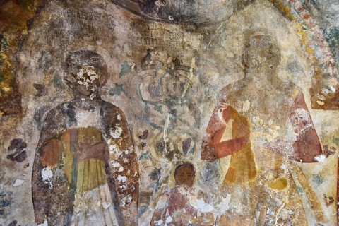 Fading frescoes on a church wall show religious figures, parents with childByzantine chapel Agios