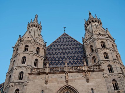 Front view of a Gothic cathedral with twin spires and a cross in the centre of the roof under a
