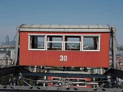 Close-up of a red cabin with the number 30 on a Ferris wheel with the city in the background,