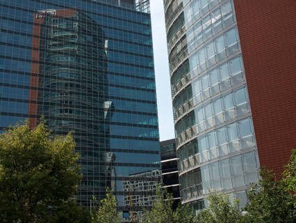 Two modern, glazed high-rise buildings with reflections and trees in the foreground, Vienna,