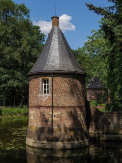 Brick round tower with lead-grey roof on a moat, surrounded by summer nature, ochtrup, münsterland,