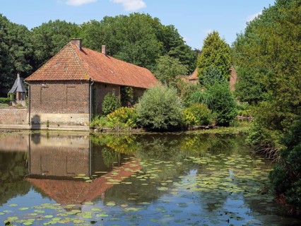 Brick building by a pond with a clear reflection, surrounded by trees and green vegetation on a