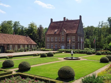 Large manor house with magnificent gardens and fountain, framed by trimmed bushes and manicured