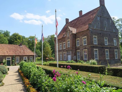 A manor house and a garden with flowerbeds and flags in the sunshine on a summer's day, ochtrup,