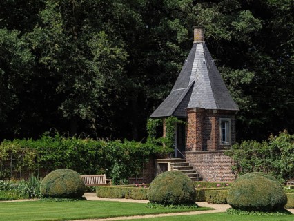 A small tower with a slate-covered roof in the middle of a well-tended garden with shrubs, green