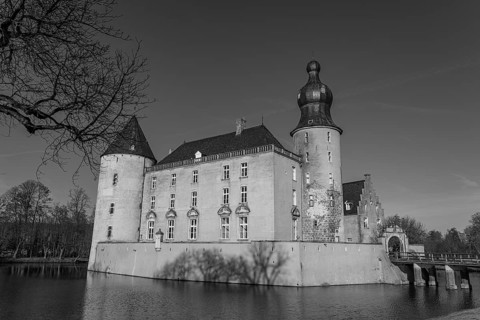A large castle with several towers and moat reflecting in the calm water, in black and white,