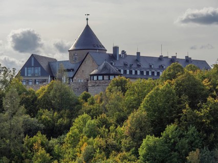 An old castle with towers surrounded by autumnal forests under a cloudy sky, Waldeck, Hesse,