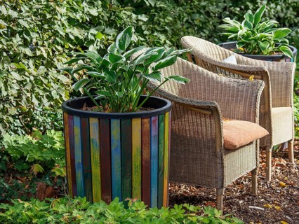 Large colourful flower pot with plants, next to it two rattan chairs in a green garden, SChermbeck
