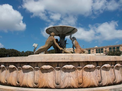 Fountain with bronze sculptures holding a bowl in front of a blue sky, valetta, mediterranean sea,