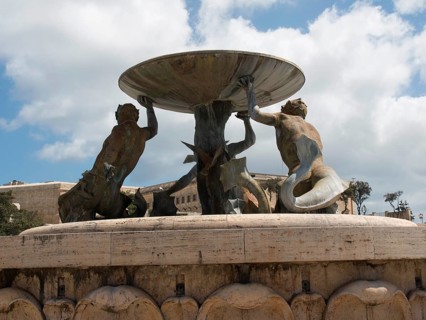 Bronze sculptures holding a large bowl of a fountain in a public square, valetta, mediterranean