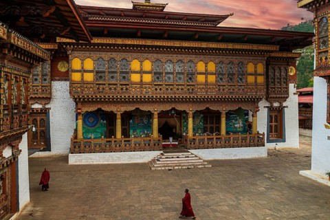 Two Buddhist monks in their traditional red dress walking in the monastery Punakha Dzong courtyard