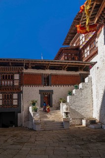 Two happy Bhutanese kids in colorful clothes walking up the stairs in the backyard of Trongsa