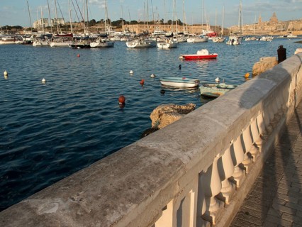 Stone balustrade along the harbour shore with many boats in the water and city in the background,