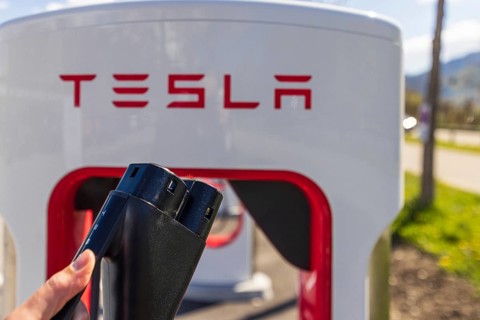 Tesla Superchargers on a parking lot, with a hand holding the CCS Type 2 plug