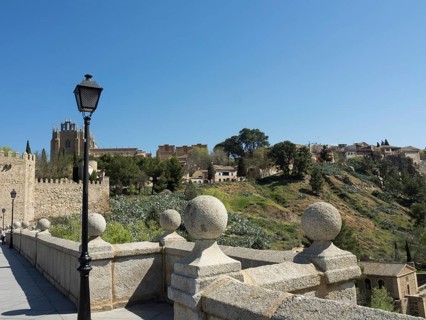 Picture of a bridge with a church in the background, surrounded by a green hilly landscape in