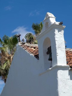 White church with a bell tower and a cross on the roof, pigeons sitting on the roof