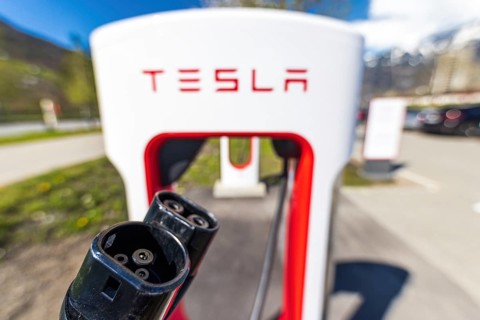 Tesla Superchargers on a parking lot, with a hand holding the CCS Type 2 plug