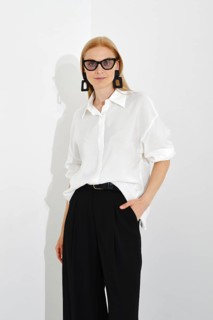 Indoor portrait of stylish blonde woman in white shirt with rolled-up sleeves and black trousers