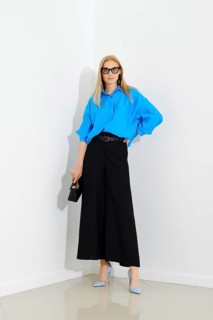 Stylish business woman in blue button down shirt and loose black skirt standing next to white wall