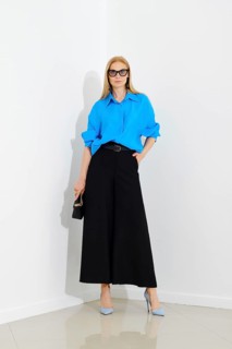 Confident woman in blue button down shirt and black maxi skirt posing over white wall