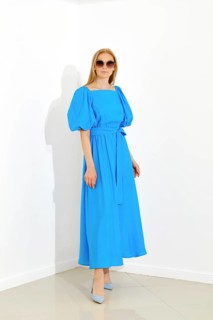 Beautiful woman with smooth blonde hair posing in bright room in long blue dress with short sleeves
