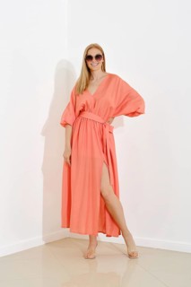 A fashion model showcases a floor-length coral dress with a v-neckline in a bright room