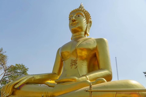 Large golden Buddha statue in lotus position in front of clear sky and trees, Pattaya, Thailand,