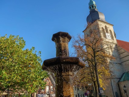 Water gushing through fountain and church tower with autumnal deciduous trees and blue sky,