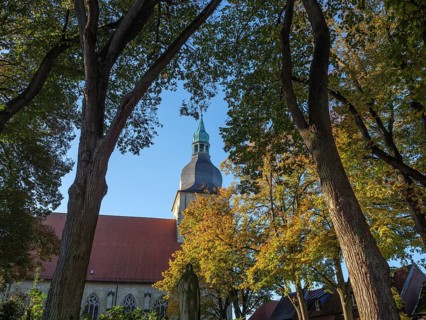 At the beginning of autumn, trees form a frame, in the centre a church with a green steeple under a