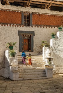 Two kids in colourful traditional clothes walking up the stairs inside Trongsa dzong