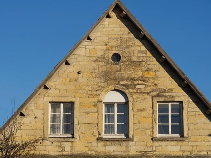 Front of an old brick house with two windows and a pointed roof gable under a blue sky, nottuln,