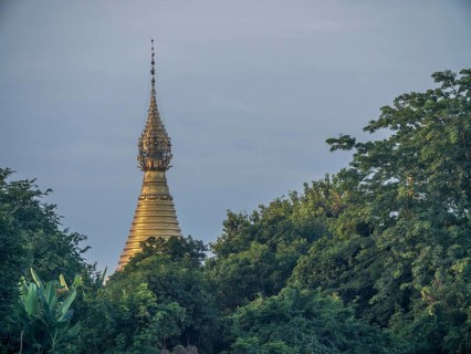 Golden stupa behind green trees at the Irrawaddy river