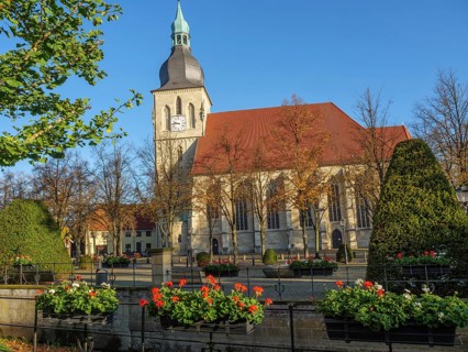A historic church with a striking church tower, surrounded by blossoming flowers and autumnal trees
