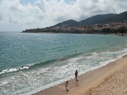 People walking along a sandy beach with a coastal town in the background, ajaccio, corsica, france