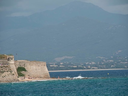 Ancient fortress wall on the coast with a view of the sea and cloudy mountains in the background,