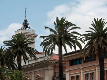 A historic building with a tower and palm trees in front of it under a slightly cloudy sky,