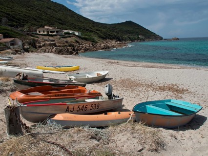 Several boats moored on the sandy beach in front of emerald green sea and green coastal hills,
